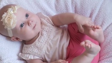 Mavi evetlerle güzel küçük bir kız çocuğu, yatağa uzanıp kameraya gülümsüyor. Yaşamın ilk yılındaki çocuk gelişimi. Çocukların korunması, evlat edinme, bebeklik kavramı