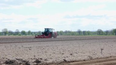 İlkbaharda traktörlü bir çiftçi tarlayı sürüyor. Ekipmanlı kırmızı çiftlik makinesinin yan görüntüsü. Bahar tarlası çalışması