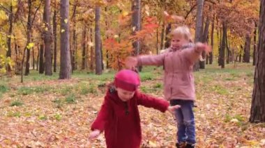 Sarı sonbahar yapraklarını fırlatan iki küçük kız parkta neşeyle gülüyordu. Autumn Park 'ta oynayan çocuklar. Sonbahar yeşilliği, açık hava eğlencesi. Sonbaharda küçük çocuk ve anaokulu çocuğu