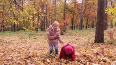 Sarı sonbahar yapraklarını fırlatan iki küçük kız parkta neşeyle gülüyordu. Autumn Park 'ta oynayan çocuklar. Sonbahar yeşilliği, açık hava eğlencesi. Sonbaharda küçük çocuk ve anaokulu çocuğu