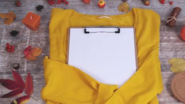 Clipboard with white blank paper, autumn leaves and yellow sweater. Autumn composition. Happy Thanksgiving and Halloween. Hello fall season