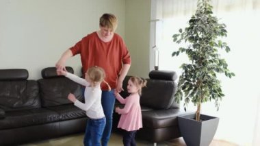Anne dadı oturma odasında dans eden küçük tatlı kızlarla eğleniyor. Mutlu bir aile. Kaygısız anne ve kız çocukları birlikte oynuyorlar evde gülüyorlar zıplayarak eğleniyorlar.