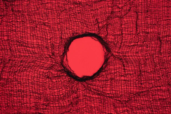 Large Textile mesh hole in the center on red background. Empty space to insert advertising content, promotion or text information. Breakthrough concept.