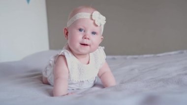 Sevimli küçük bir kız bebek yatakta yüzüstü yatar ve kameraya bakar ve gülümser. Erken bebek gelişimi.