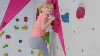 Cesur çocuk sarışın kız, tırmanma egzersizlerinde yapay duvara tırmanıyor. Çocukluk ve ekstrem spor kavramı.