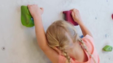 Cesur çocuk sarışın kız, tırmanma egzersizlerinde yapay duvara tırmanıyor. Çocukluk ve ekstrem spor kavramı.