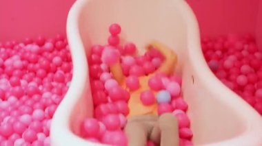 Küçük mutlu sarışın beyaz kız pembe plastik toplarla banyoda uzanıyor ve onlarla oynuyor. Yakın plan, Mutlu çocukluk.