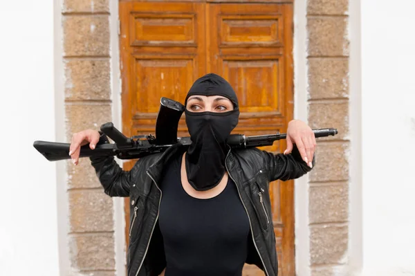 En vit flicka i en balaklava håller ett gevär på sina axlar. Flicka med ett vapen. Brott och straff. — Stockfoto