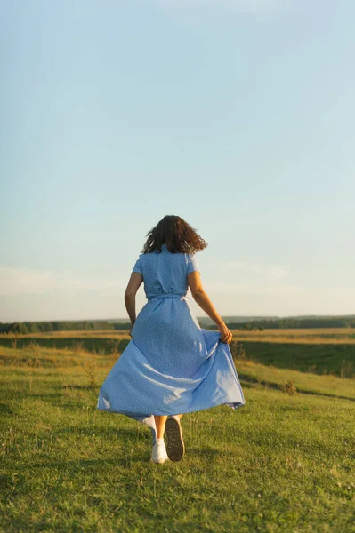 Mavi elbiseli beyaz bir esmer gün batımında kuyruklu yıldızdan kaçar..