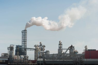 Modern bir fabrikanın üstündeki beyaz bacadan duman çıkıyor. Çevre kirliliği.