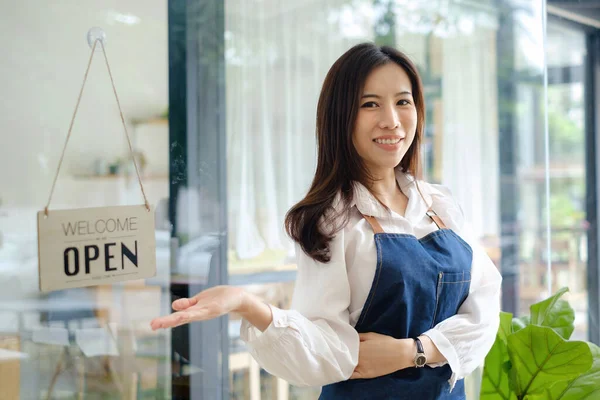 Γυναίκα ιδιοκτήτρια με χαμόγελο γυρίζει ένα σημάδι από κλειστό σε ανοιχτό. Έννοια της ελεύθερης εργασίας και της επιχειρηματικότητας ΜΜΕ. — Φωτογραφία Αρχείου