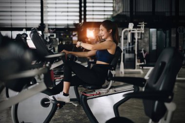 Mutlu genç kadın gülümsüyor ve spor bisikletçiliği ile spor yapıyor..