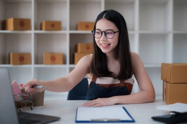 Asyalı küçük işletme sahibi ev ofisinde çalışıyor. Ticari perakende pazarı ve çevrimiçi pazarlama dağıtımı, KOBİ e-ticaret kavramı.