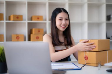 Asyalı küçük işletme sahibi ev ofisinde çalışıyor. Ticari perakende pazarı ve çevrimiçi pazarlama dağıtımı, KOBİ e-ticaret kavramı.