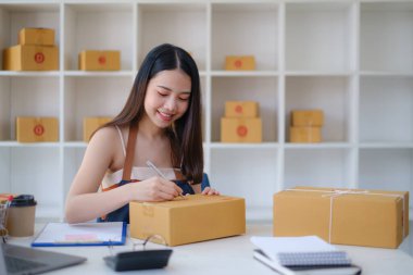 Asyalı küçük işletme sahibi ev ofisinde çalışıyor. Ticari perakende pazarı ve çevrimiçi pazarlama dağıtımı, KOBİ e-ticaret kavramı.