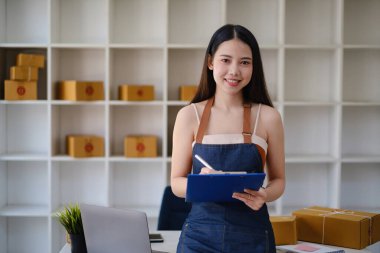 Asyalı küçük işletme sahibi ev ofisinde çalışıyor. Ticari perakende pazarı ve çevrimiçi pazarlama dağıtımı, KOBİ e-ticaret kavramı.