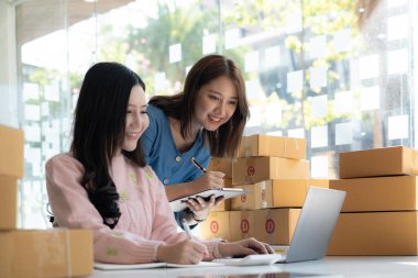 Asyalı küçük işletme sahibi ev ofisindeki arkadaşıyla birlikte çalışıyor. Ticari perakende pazarı ve çevrimiçi pazarlama dağıtımı, KOBİ e-ticaret kavramı.