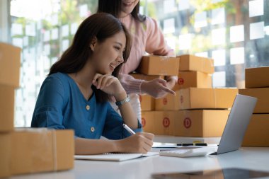 Asyalı küçük işletme sahibi ev ofisindeki arkadaşıyla birlikte çalışıyor. Ticari perakende pazarı ve çevrimiçi pazarlama dağıtımı, KOBİ e-ticaret kavramı.