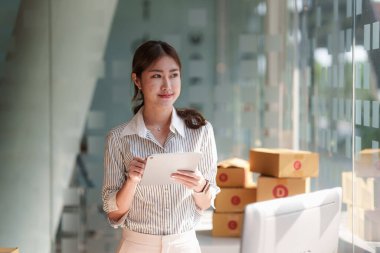 Asyalı küçük işletme sahibi ev ofisinde çalışıyor. Ticari perakende pazarı ve çevrimiçi pazarlama dağıtımı, KOBİ e-ticaret kavramı.