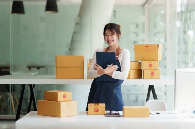 Asyalı küçük işletme sahibi ev ofisinde çalışıyor. Ticari perakende pazarı ve çevrimiçi pazarlama dağıtımı, KOBİ e-ticaret kavramı.