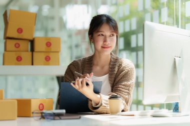 Asyalı küçük işletme sahibi ev ofisinde çalışıyor. Ticari perakende pazarı ve çevrimiçi pazarlama dağıtımı, KOBİ e-ticaret kavramı.