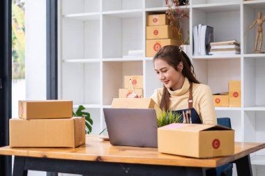 Asyalı küçük işletme sahibi ev ofisinde çalışıyor. Ticari perakende pazarı ve çevrimiçi pazarlama dağıtımı, KOBİ e-ticaret kavramı.