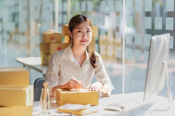 Asyalı küçük işletme sahibi ev ofisinde çalışıyor. Ticari perakende pazarı ve çevrimiçi pazarlama dağıtımı, KOBİ e-ticaret kavramı.
