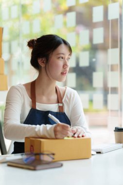 Asyalı küçük işletme sahibi ev ofisinde çalışıyor. Ticari perakende pazarı ve çevrimiçi pazarlama dağıtımı, KOBİ e-ticaret kavramı.