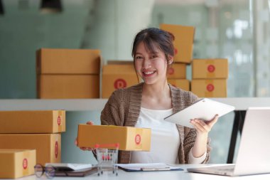 Asyalı küçük işletme sahibi ev ofisinde çalışıyor. Ticari perakende pazarı ve çevrimiçi pazarlama dağıtımı, KOBİ e-ticaret kavramı.