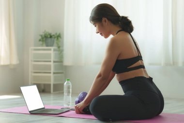 Evde dizüstü bilgisayar dersinde yoga eğitimi alan genç bir kadın. Sakinlik ve rahatlama konsepti.