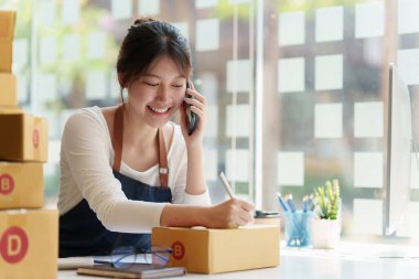 Asyalı küçük işletme sahibi ev ofisinde çalışıyor. Ticari perakende pazarı ve çevrimiçi pazarlama dağıtımı, KOBİ e-ticaret kavramı.