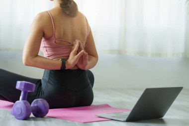 Evde dizüstü bilgisayar dersinde yoga eğitimi alan genç bir kadın. Sakinlik ve rahatlama konsepti.