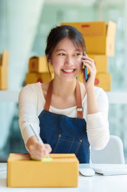 Asyalı küçük işletme sahibi ev ofisinde çalışıyor. Ticari perakende pazarı ve çevrimiçi pazarlama dağıtımı, KOBİ e-ticaret kavramı.