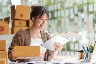 Asyalı küçük işletme sahibi ev ofisinde çalışıyor. Ticari perakende pazarı ve çevrimiçi pazarlama dağıtımı, KOBİ e-ticaret kavramı.