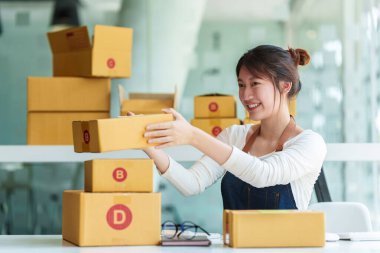 Asyalı küçük işletme sahibi ev ofisinde çalışıyor. Ticari perakende pazarı ve çevrimiçi pazarlama dağıtımı, KOBİ e-ticaret kavramı.