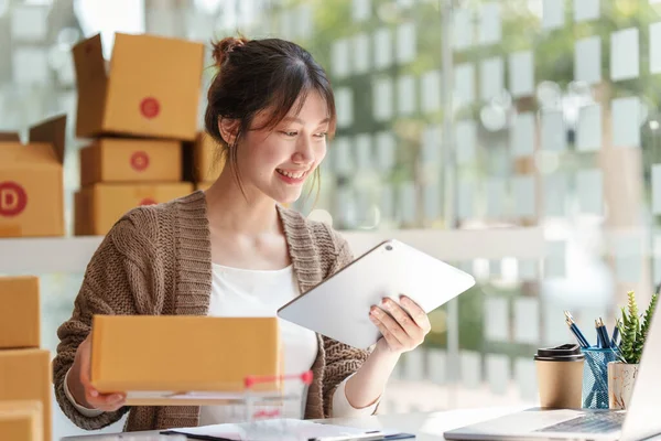 Asyalı küçük işletme sahibi ev ofisinde çalışıyor. Ticari perakende pazarı ve çevrimiçi pazarlama dağıtımı, KOBİ e-ticaret kavramı.