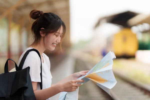 Ung resenär kvinna tittar på kartor planerar resa på tågstationen. Sommar och resor livsstil koncept. — Stockfoto