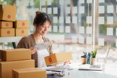 Asyalı küçük işletme sahibi ev ofisinde çalışıyor. Ticari perakende pazarı ve çevrimiçi pazarlama dağıtımı, KOBİ e-ticaret kavramı.