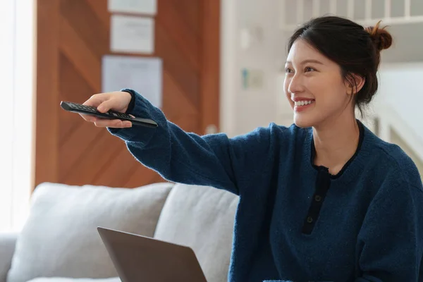 Spännande ung asiatisk kvinna tittar på tv-program med fjärrkontroll. Livsstil och tillbringa fritid hemma. — Stockfoto