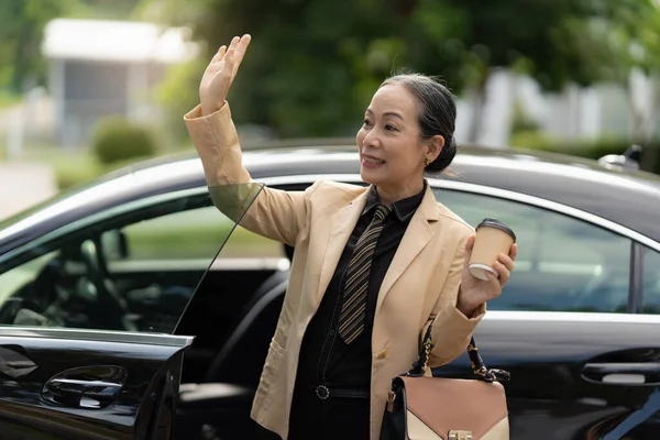 Portrait of Asian Senior Business woman step out luxury car while come to office. Account and Finance concept
