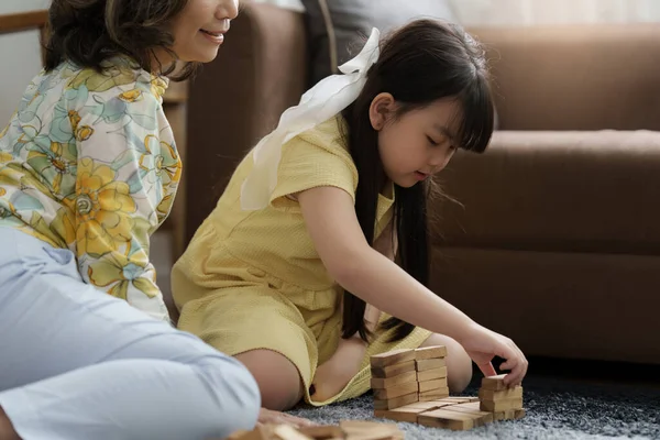 Girl playing wooden jenga constructor with grandmother at home. Leisure activities for children at home