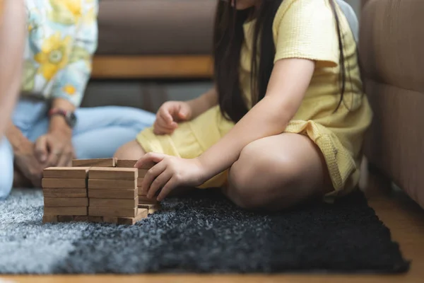 Girl playing wooden jenga constructor with grandmother at home. Leisure activities for children at home