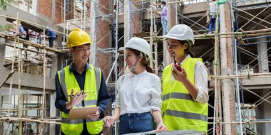 Structural engineer and architect discussing and working with blueprints at the outdoors construction site.