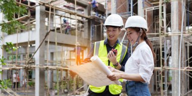 Structural engineer and architect discussing and working with blueprints at the outdoors construction site.