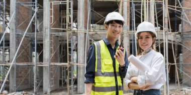 Structural engineer and architect discussing and working with blueprints at the outdoors construction site.