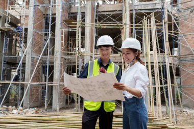 Structural engineer and architect discussing and working with blueprints at the outdoors construction site.