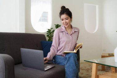 Asian woman using laptop and sitting on sofa at home office.