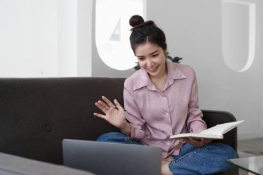 Asian woman using laptop and sitting on sofa at home office.