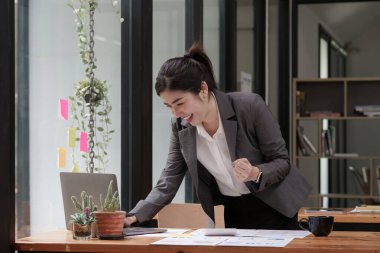 Happy Asian woman using laptop computer while have a good news working at office