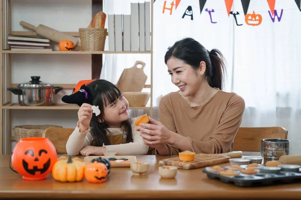 ハロウィンの若い女の子と母親がテーブルの上でお菓子やカップケーキを作っています ハッピーハロウィーンの日 — ストック写真
